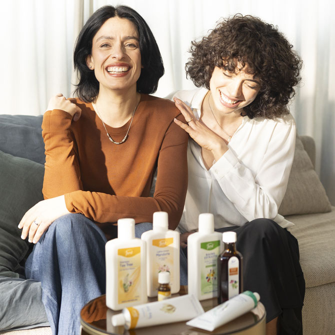 La padrona di casa e la consulente Just sorridono sedute sul divano, con prodotti Just in primo piano.
