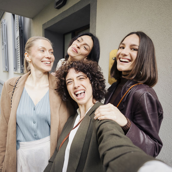 Quattro amiche sorridenti scattano un selfie all’ingresso di casa, pronte per un Party Just.